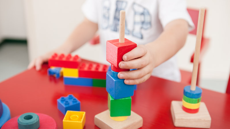 Ein Kindergartenkind spielt mit bunten, stapelbaren Holzbausteinen.